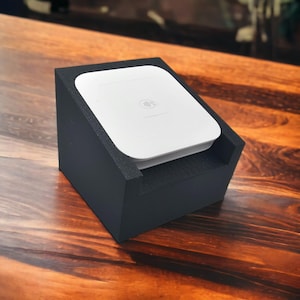 May include: A white square-shaped credit card reader sits in a black foam stand. The reader has a contactless symbol on it.