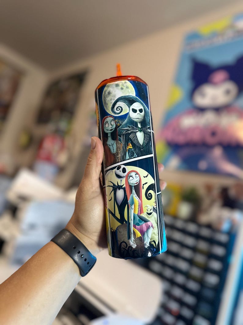 May include: A black and white stainless steel tumbler with a colorful image of Jack Skellington and Sally from the Nightmare Before Christmas. The tumbler has a black lid with a clear straw.