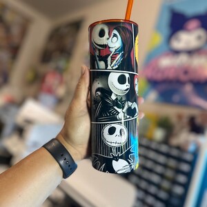 May include: A black and white tumbler with a graphic of Jack Skellington and Sally from the Nightmare Before Christmas. The tumbler has a black lid and an orange straw.