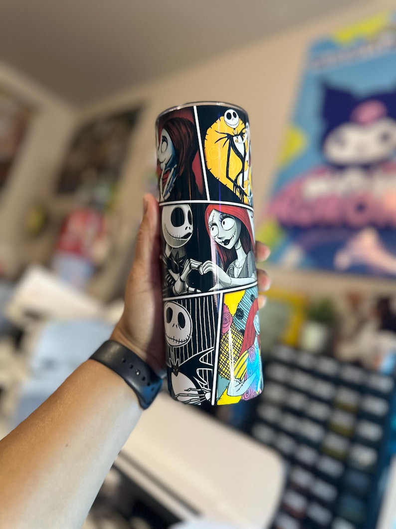 May include: A black and white tumbler with a comic book style design featuring characters from The Nightmare Before Christmas. The characters include Jack Skellington, Sally, and Oogie Boogie.