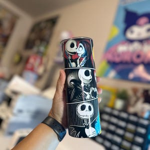 May include: A black and white stainless steel tumbler with a graphic print of Jack Skellington and Sally from the Nightmare Before Christmas movie. The tumbler has a black lid and a black straw.