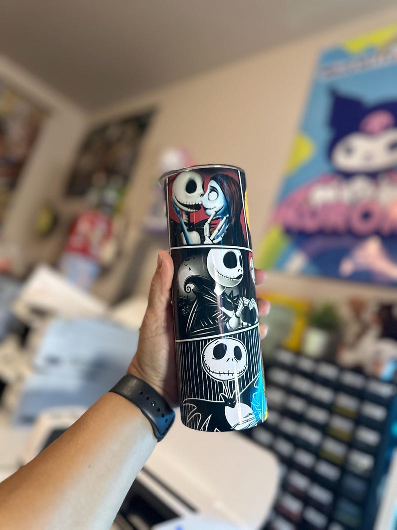 May include: A black and white stainless steel tumbler with a graphic print of Jack Skellington and Sally from the Nightmare Before Christmas movie. The tumbler has a black lid and a black straw.