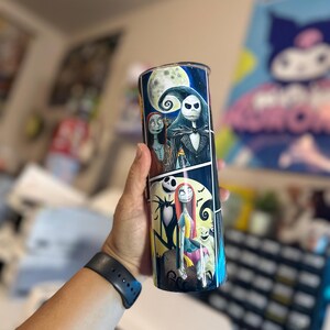 May include: A black and white tumbler with a colorful image of Jack Skellington and Sally from the Nightmare Before Christmas. The image is a comic book style with a moon and stars in the background.