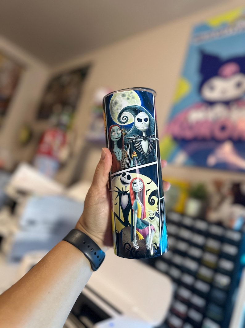 May include: A black and white tumbler with a colorful image of Jack Skellington and Sally from the Nightmare Before Christmas. The image is a comic book style with a moon and stars in the background.