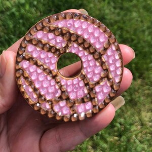 Op de afbeelding: Een roze en bruine donutvormige harsbedel met een textuur. De bedel is versierd met een swirl-patroon.