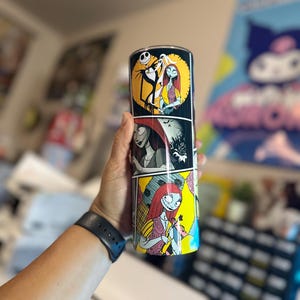 May include: A black and white stainless steel tumbler with a colorful comic book style design featuring characters from the Nightmare Before Christmas. The tumbler features Jack Skellington and Sally.