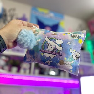 May include: A light blue and white zippered pouch with a rainbow, stars, and clouds design. The pouch features a cartoon dog with the text "Cinnamoroll".