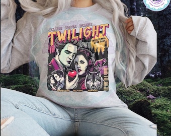 May include: A light gray sweatshirt featuring a graphic from the movie "Twilight." The design includes illustrations of Edward Cullen, Bella Swan, and a wolf, with the text "Twilight" and "The Eternal Love Saga."