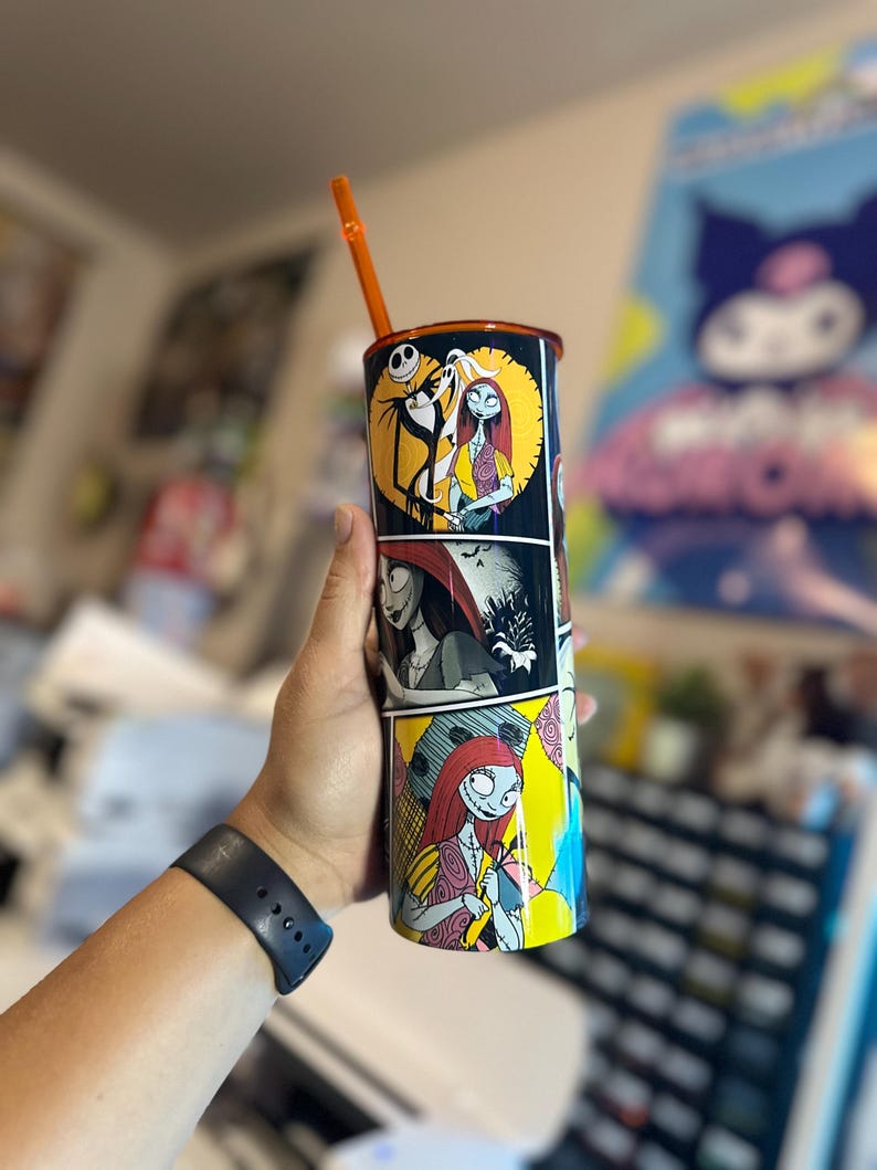 May include: A black and white tumbler with a colorful comic book style design featuring Jack Skellington and Sally from The Nightmare Before Christmas. The tumbler has an orange straw.