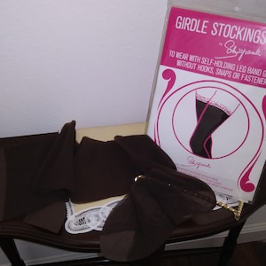 Puede incluir: Un paquete marrón de medias con el texto "GIRDLE STOCKINGS by Shigpaute" y "TO WEAR WITH SELF-HOLDING LEG BAND GIRDLES WITHOUT HOOKS, SNAPS OR FASTENERS" en la parte delantera. El paquete está sobre una mesa de madera.