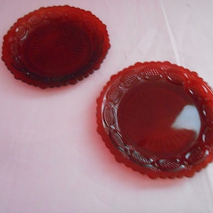 May include: Two red glass plates with a scalloped edge and a raised design. The plates are on a white surface.
