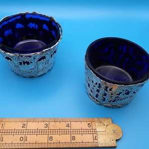 May include: Two small, silver-plated bowls with intricate designs. The bowls are lined with cobalt blue glass.