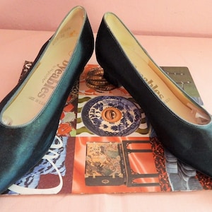 May include: A pair of teal blue satin pumps with a low heel. The shoes are made by the brand "Deables" and are made in the USA.