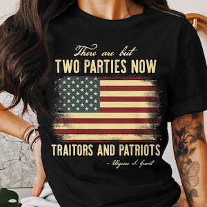 Puede incluir: Camiseta negra con un diseño desgastado de la bandera estadounidense y el texto "There are but TWO PARTIES NOW Traitors and Patriots - Ulysses S. Grant." La camiseta tiene cuello redondo y mangas cortas.