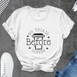 Op de afbeelding: Wit T-shirt met een zwarte afbeelding met de tekst "No Talkie Before Coffee" met een koffiekopje-icoon.