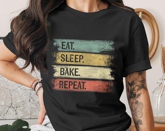 Puede incluir: Camiseta negra con la frase "EAT. SLEEP. BAKE. REPEAT." en un diseño desgastado y colorido. Las palabras están dispuestas en franjas horizontales azules, amarillas, blancas y rojas. Una camiseta cómoda para los amantes de la repostería.