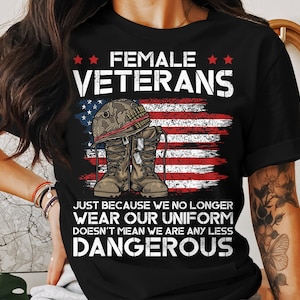 Puede incluir: Camiseta negra con el texto "FEMALE VETERANS" sobre un diseño de la bandera estadounidense y botas militares. La camiseta también incluye el texto "JUST BECAUSE WE NO LONGER WEAR OUR UNIFORM DOESN'T MEAN WE ARE ANY LESS DANGEROUS."