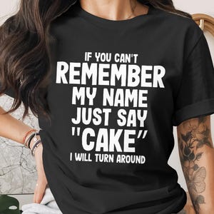 May include: Black t-shirt with white text: "IF YOU CAN'T REMEMBER MY NAME JUST SAY 'CAKE' I WILL TURN AROUND." The shirt has short sleeves and is being worn by a person. The text is in a bold, sans-serif font.