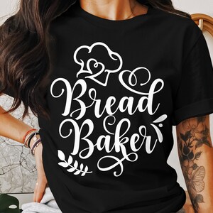 May include: Black t-shirt featuring the text "Bread Baker" in white cursive script. The design includes a chef's hat and a sprig of leaves. The shirt is a casual style.