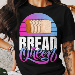 May include: Black t-shirt featuring a colorful graphic. The design includes a loaf of bread above the words "BREAD Queen" in white and a cursive font. The background is a gradient of pink, purple, and blue, resembling a sunset.