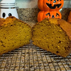 May include: Two slices of pumpkin bread, cut in half, are displayed on a wire rack. The bread is a vibrant orange color and has a soft, crumbly texture.