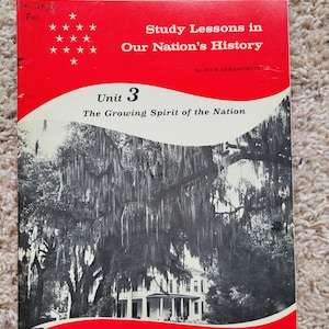 May include: A red and white book titled "Study Lessons in Our Nation's History" by Jack Abramowitz. The book is open to Unit 3, "The Growing Spirit of the Nation". The cover features a black and white photograph of a house with a large tree in the foreground.