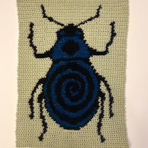 May include: A crocheted wall hanging featuring a blue and black beetle with a spiral design on its back. The beetle is on a light green background.