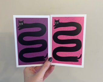 May include: Two postcards with a black cat illustration. The cat is stretched out in a long, wavy shape. One postcard has a purple background and the other has a pink background.