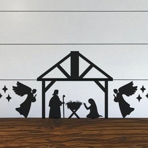 May include: Black silhouette of a nativity scene with a manger, Mary, Joseph, and two angels with stars above them. The scene is on a white wood background.