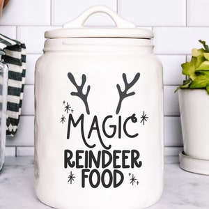 Op de afbeelding: Witte keramische pot met een zwart rendiergewei-ontwerp en de tekst "*MAGIC* REINDEER FOOD*" aan de voorkant.