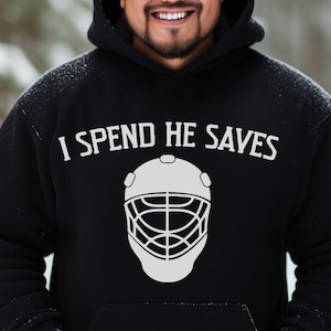 May include: Black hoodie with white text that reads "I spend he saves" and a white hockey goalie mask graphic.