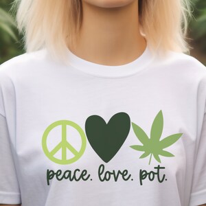 Puede incluir: Camiseta blanca con un símbolo de paz verde, un corazón verde y una hoja de marihuana verde. El texto "peace. love. pot." está impreso debajo de los símbolos.