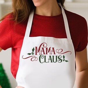 Op de afbeelding: Witte schort met de tekst "Mama Claus" in rood en groen met een kerststerontwerp.