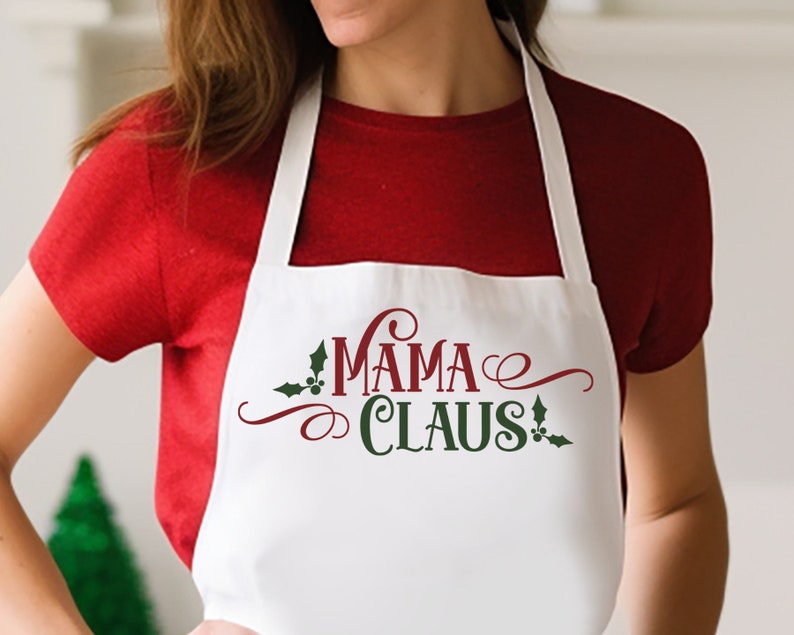 Op de afbeelding: Witte schort met de tekst "Mama Claus" in rood en groen met een kerststerontwerp.