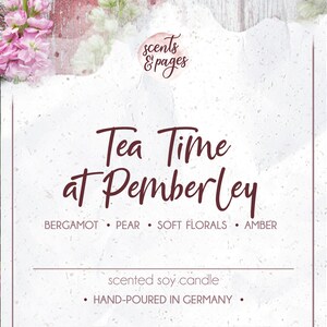 May include: A white card with the text "Tea Time at Pemberley" in maroon script. The card is surrounded by pink and white flowers and greenery. The text "scented soy candle" and "HAND-POURED IN GERMANY" is also on the card. The candle is scented with bergamot, pear, soft florals, and amber.