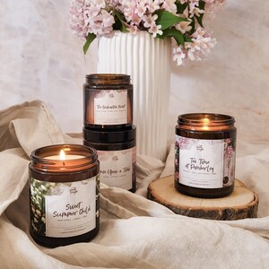 May include: Four amber glass candle jars with labels and floral designs. The candles are lit and have a warm glow. The labels read "The Enchanted Forest", "Once Upon a Time", "Sweet Summer Child", and "Tea Time at Pemberley".