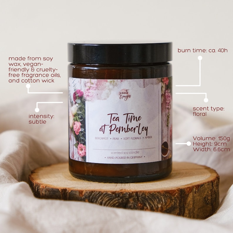 May include: A brown glass candle jar with a floral design label. The label reads "Tea Time at Pemberley" with the scent notes "Bergamot, Pear, Soft Florals, Amber". The candle is hand-poured in Germany and is a scented soy candle. The candle is sitting on a wooden slice.