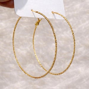 Puede incluir: Una taza de cerámica blanca con asa negra y el texto "But First, Coffee" en negrita negra. La taza se encuentra sobre un fondo borroso, sugiriendo un ambiente acogedor.