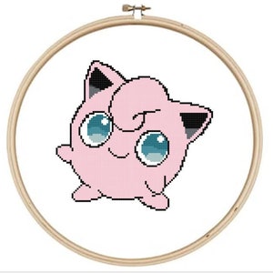 May include: A pink and black cartoon character with big eyes and a curled tail. The character is in a circular wooden embroidery hoop.