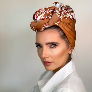 May include: A woman wearing a turban-style head covering. The head covering is a mix of brown, tan, and white fabrics with a floral pattern. She is wearing a white button-down shirt.
