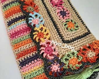 Puede incluir: Bolso de crochet hecho a mano con forma rectangular y cierre de solapa. El bolso presenta un colorido estampado de rayas en la parte delantera y un diseño floral en la solapa. El bolso tiene una borla verde y una correa trenzada.