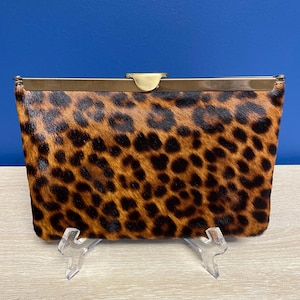May include: A brown and black leopard print clutch purse with a gold metal clasp.