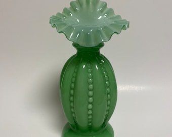 May include: A green glass vase with a ruffled top and a beaded design. The vase is made of a translucent glass and has a delicate, feminine look.