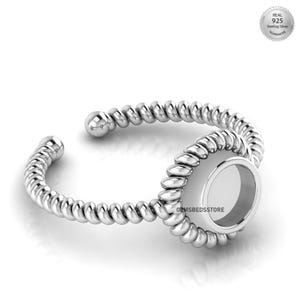 May include: A silver-colored ring with a twisted rope design. The ring features an open design with a circular setting in the center. The ring is made of sterling silver, as indicated by the "Real 925 Sterling Silver Guarantee" stamp.