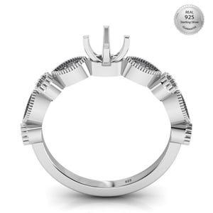 Puede incluir: Un anillo de plata con un diseño decorativo. El anillo presenta un engaste de garras y una serie de formas estilizadas y repetitivas alrededor de la banda. El anillo está estampado con "925" e incluye un sello de "Real 925 Sterling Silver Guarantee".