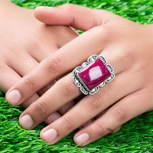 May include: A silver ring with a large, rectangular, pink gemstone set in a decorative silver frame.