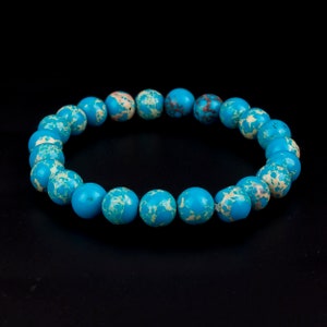 May include: A beaded bracelet featuring round, turquoise-colored beads with cream and brown marbling. The bracelet is displayed against a black background, highlighting the vibrant colors and natural stone pattern. This accessory is suitable for everyday wear.