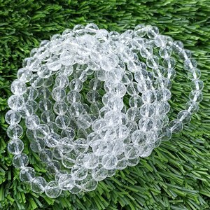 May include: A strand of clear faceted crystal beads. The beads are round and have a smooth, polished finish. The beads are strung together on a clear thread.