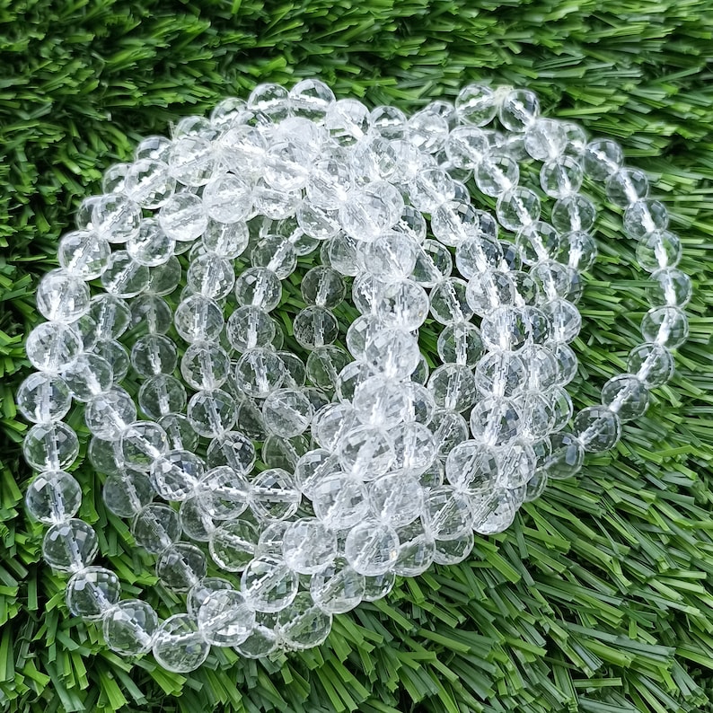 May include: A strand of clear faceted crystal beads. The beads are round and have a smooth, polished finish. The beads are strung together on a clear thread.