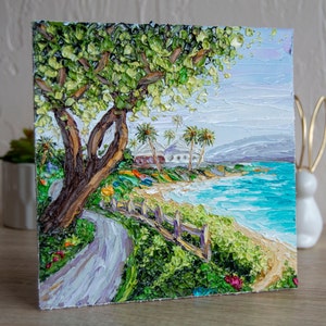 K&ouml;nnte beinhalten: Ein Gem&auml;lde, das eine tropische Strandszene mit einem gro&szlig;en gr&uuml;nen Baum im Vordergrund, einem wei&szlig;en Geb&auml;ude in der Ferne und einem blauen Meer mit Wellen zeigt. Das Gem&auml;lde ist in einem dicken, strukturierten Stil ausgef&uuml;hrt.